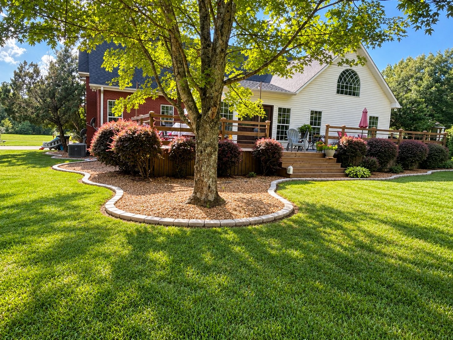 Curved planting beds with paver borders and shaped shrubs around a home and mature tree